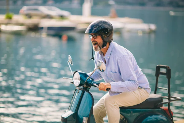 Mature man driving motor scooter in marina near the sea. — Stock Photo, Image