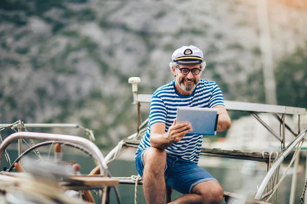 Maturo uomo in piedi sul ponte della sua barca e utilizzando digitale ta — Foto Stock