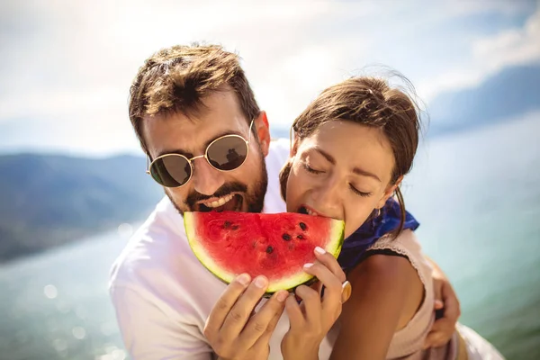 Jong glimlachen paar eten watermeloen op het strand het hebben van plezier. — Stockfoto