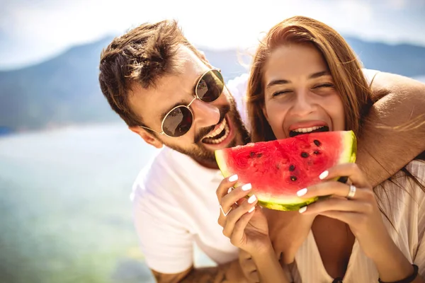 Молодая улыбающаяся пара, кушающая арбуз на пляже. — стоковое фото