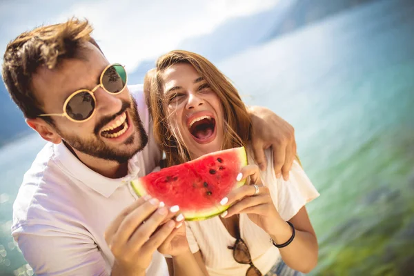 Joven pareja sonriente comiendo sandía en la playa divirtiéndose. — Foto de Stock