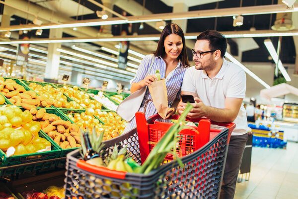 Photo of young cheerful loving couple in supermarket with shoppi