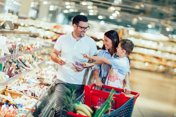Happy family with child and shopping cart buying food at grocery — Stock Photo, Image
