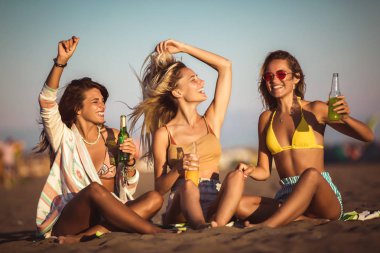 Sahilde oturan mutlu genç kadınlar. Arkadaş grubu enjoyin