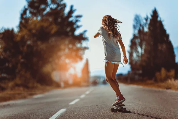 Jonge sportieve vrouw rijden op het skateboard op de weg. — Stockfoto