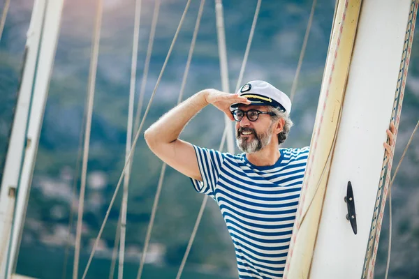 Reifer Mann steht lachend am Steuer eines Segelbootes auf hoher See — Stockfoto