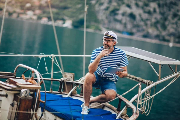 Maturo uomo in piedi sul ponte della sua barca e utilizzando digitale ta — Foto Stock