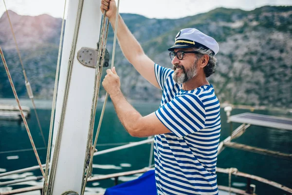 Homem maduro de pé e rindo do leme do veleiro no mar — Fotografia de Stock