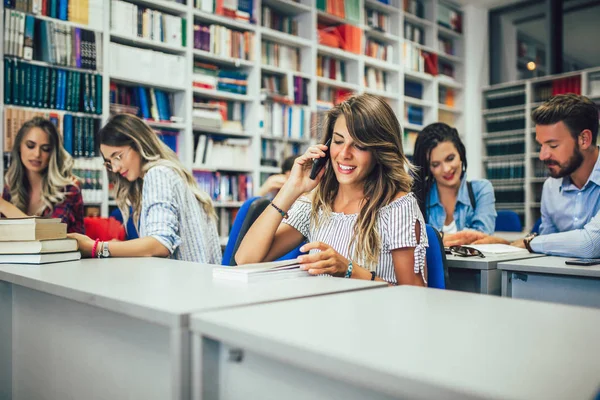 Portrait of a beautiful student using phone in a library — Stock Photo, Image