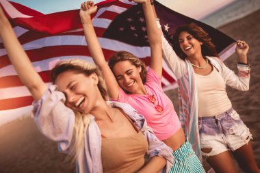 Genç arkadaşlar kumsalda Amerikan bayrağı taşıyor.
