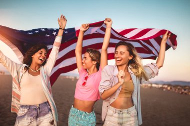 Genç arkadaşlar kumsalda Amerikan bayrağı taşıyor.