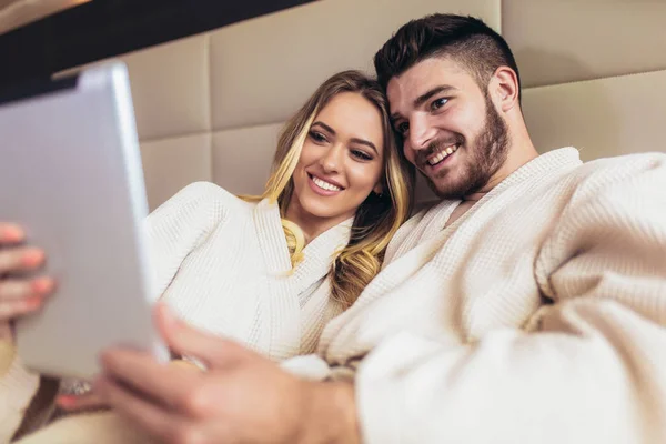 Pareja feliz usando tableta digital mientras están acostados juntos en la cama en — Foto de Stock