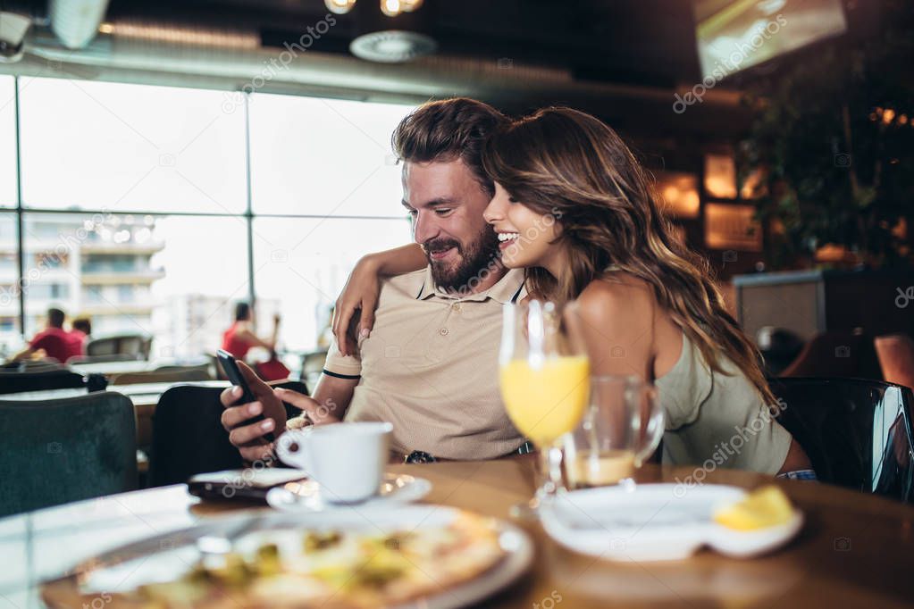 Happy couple with smartphone drinking tea or coffee at cafe