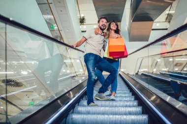 Yürüyen merdivenle aşağı gidiyor alışveriş çantaları ile mutlu genç çift