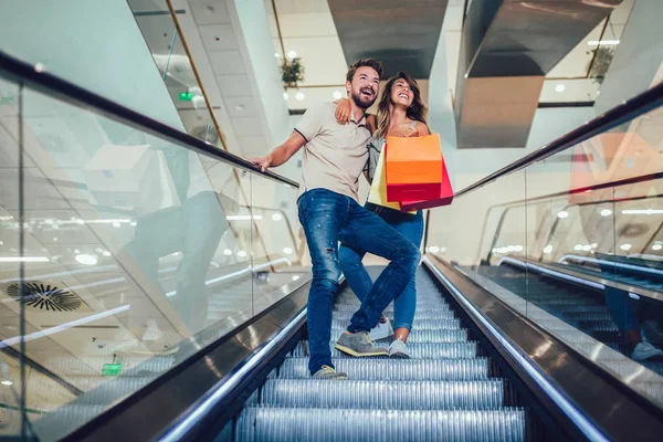 エスカレーターで下りる買い物袋を持つ幸せな若いカップル — ストック写真