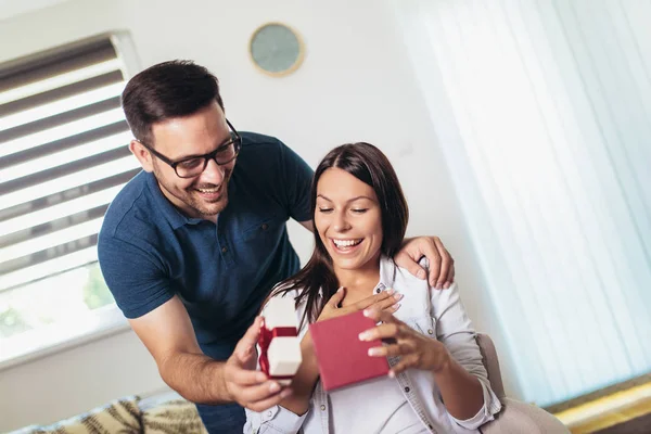 Uśmiechnięty mężczyzna zaskakuje swoją dziewczynę prezentem w domu — Zdjęcie stockowe