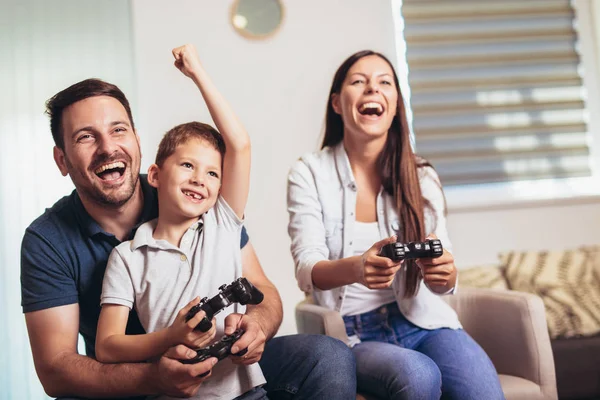 Familia sonriente sentada en el sofá jugando videojuegos — Foto de Stock