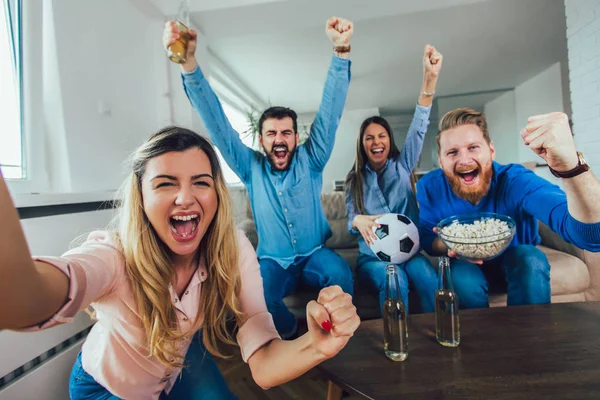 Happy friends or football fans watching soccer on tv and celebra