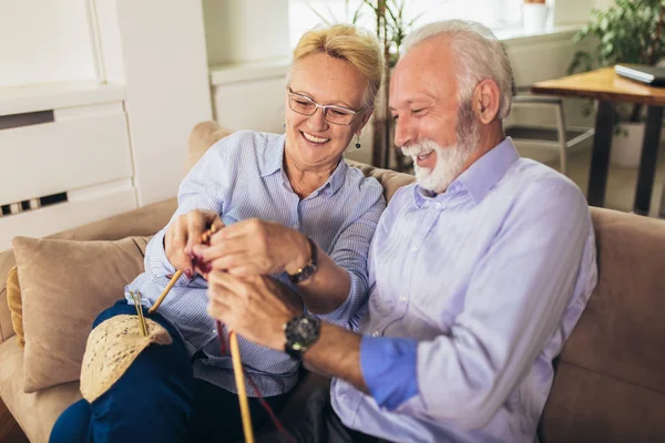 Senior woman teaching her husband the art of knitting woollen cl