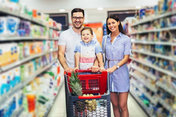 Família feliz com criança e carrinho de compras comprando comida no supermercado — Fotografia de Stock