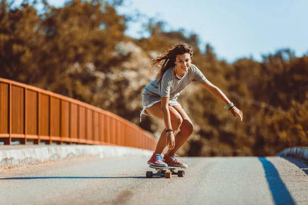 Jonge sportieve vrouw rijden op het skateboard op de weg. — Stockfoto