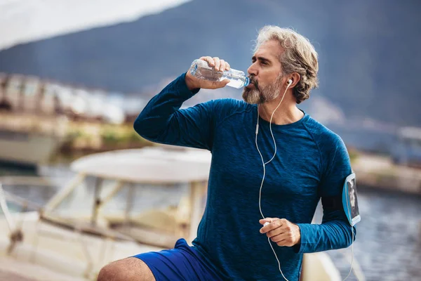 Encaixe o homem sênior sedento que bebe a água antes de correr. Velho activo — Fotografia de Stock