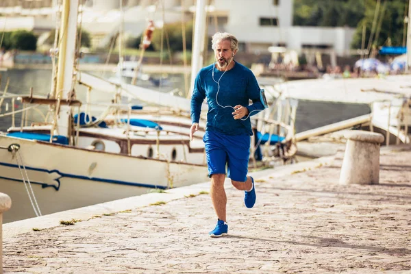 Actieve senior man joggen op de pier op een zonnige dag — Stockfoto