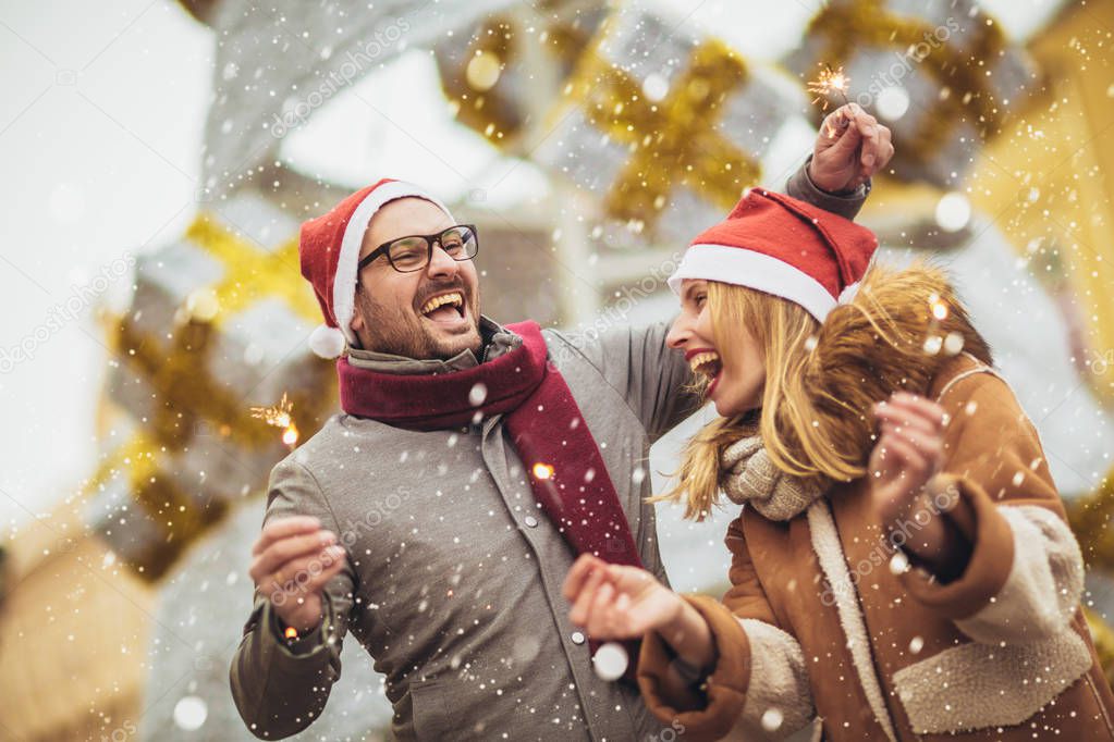 Young beautiful couple with Santa hats holding sprinklers in the