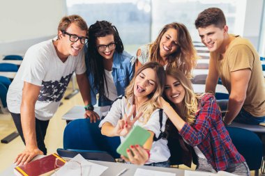 Sınıfta akıllı telefonda grup selfie'si yapan neşeli öğrenciler.
