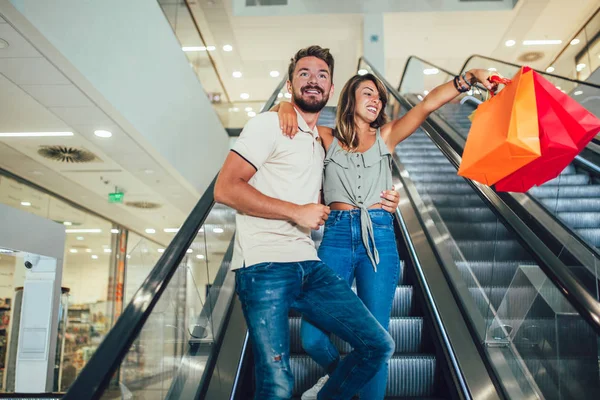 エスカレーターで買い物袋を持つ幸せな若いカップル。S — ストック写真