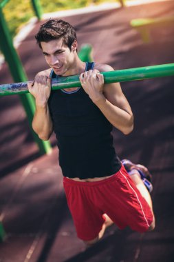 Fitness adamı dışarıda yatay barda egzersiz yapıyor.