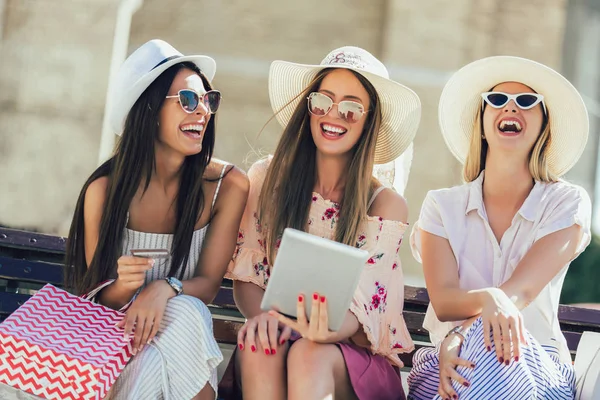 Три дівчини з різнокольоровими сумками з використанням цифрового планшета і — стокове фото