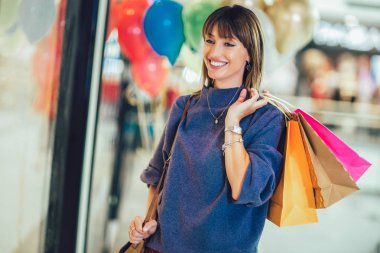 Güzel kız gülümsüyor, alışveriş torbalarını tutuyor.