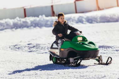 Çocuk kış manzarasında kar motosikleti sürüyor.