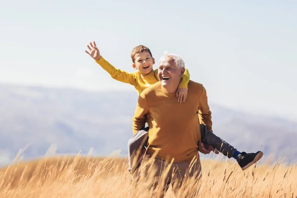 Grandson piggyback with his grandfather in autumn. — Stock Photo, Image