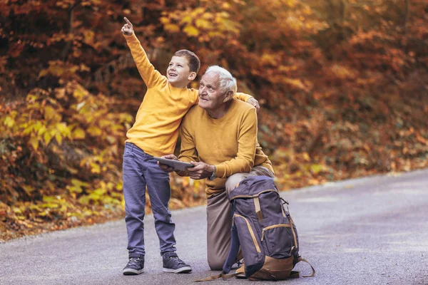 Senior man die kaart leest op digitale tablet met kleinzoon in het bos — Stockfoto