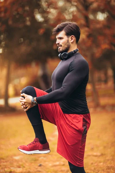 Esporte homem que se estende no parque outono, fazendo exercícios . — Fotografia de Stock