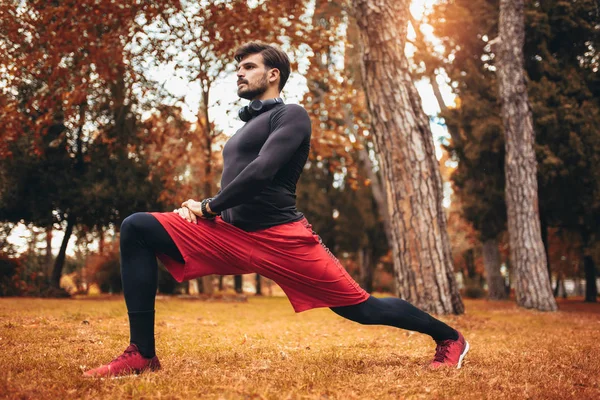 Esporte homem que se estende no parque outono, fazendo exercícios . — Fotografia de Stock