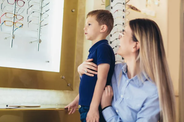 Gelukkig moeder kiezen bril frame voor haar zoon in optische st — Stockfoto