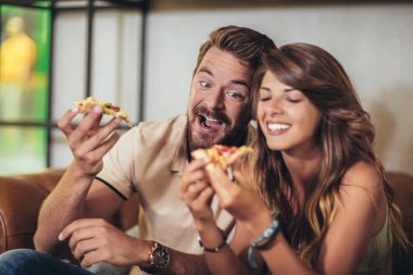 Modern kafede pizza yiyen bir çift. Gülüyorlar ve yemek yiyorlar.