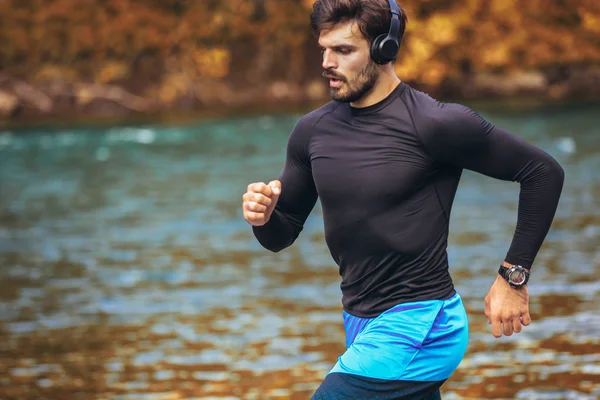 Knappe jonge man joggen op de oever van de rivier — Stockfoto