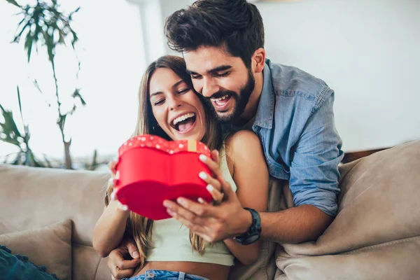 Glückliches Paar mit Geschenkbox, das sich zu Hause umarmt. schöner Mann ist givi — Stockfoto