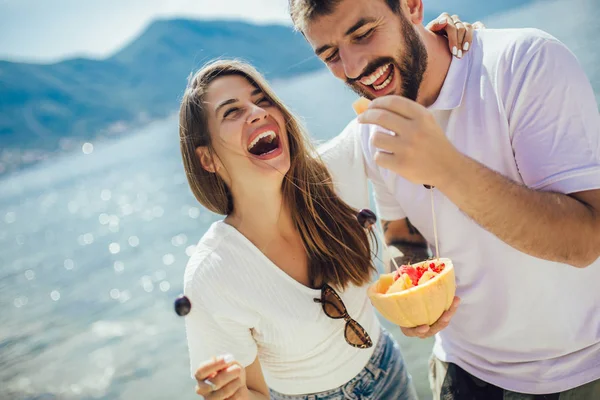 Pareja joven comiendo fruta en la playa- fiesta de verano con un amigo — Foto de Stock