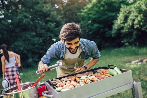 Young man preparing barbecue for friends outdoor