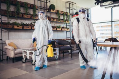 Tehlikeli madde giysileri içindeki profesyonel işçiler kafenin veya restoranın iç kısımlarını dezenfekte ediyorlar, salgın hastalık riski, koronavirüs.