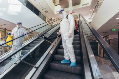 Tehlikeli madde giysileri içinde profesyonel işçiler alışveriş merkezinin iç kısımlarını dezenfekte ediyor, salgın hastalık riski, koronavirüs...