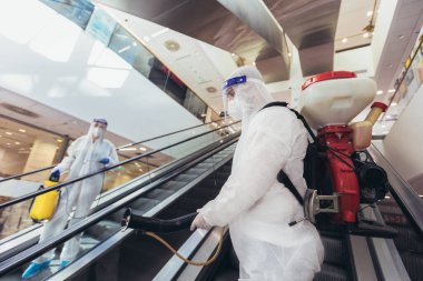 Tehlikeli madde giysileri içinde profesyonel işçiler alışveriş merkezinin iç kısımlarını dezenfekte ediyor, salgın hastalık riski, koronavirüs...