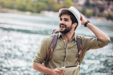 Elinde dijital tabletle arka planda teknelerle turistik bir tatil köyünün limanında yürüyen genç adam..