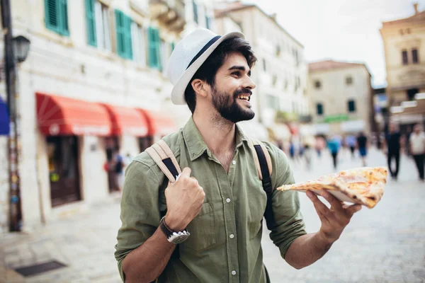 若い男は食欲をそそるピザの一部を食べます 空腹の男は彼の手にピザの一部を保持しています 彼を見て それを食べるつもりです ファーストフード — ストック写真