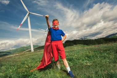 Süper kahraman çocuk rüzgar çiftliğinin önünde. Küçük çocuk süper kahramanı oynuyor..